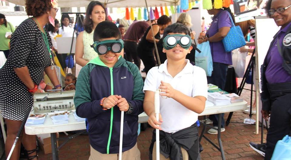 Two young boys try on the vision simulators and practice using white canes.